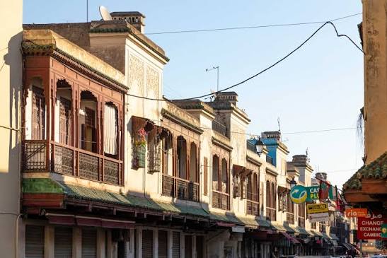 A street in Morocco's old Jewish quarter — wooden balconies, carved facades and a centuries-old gate frame a scene unchanged in its essentials for five hundred years